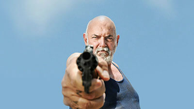 Actor Jamie Dunn in his role in the Short Film 'True Love'. In this image, he's set against a bright blue sky and menacingly points a pistol at the viewer.